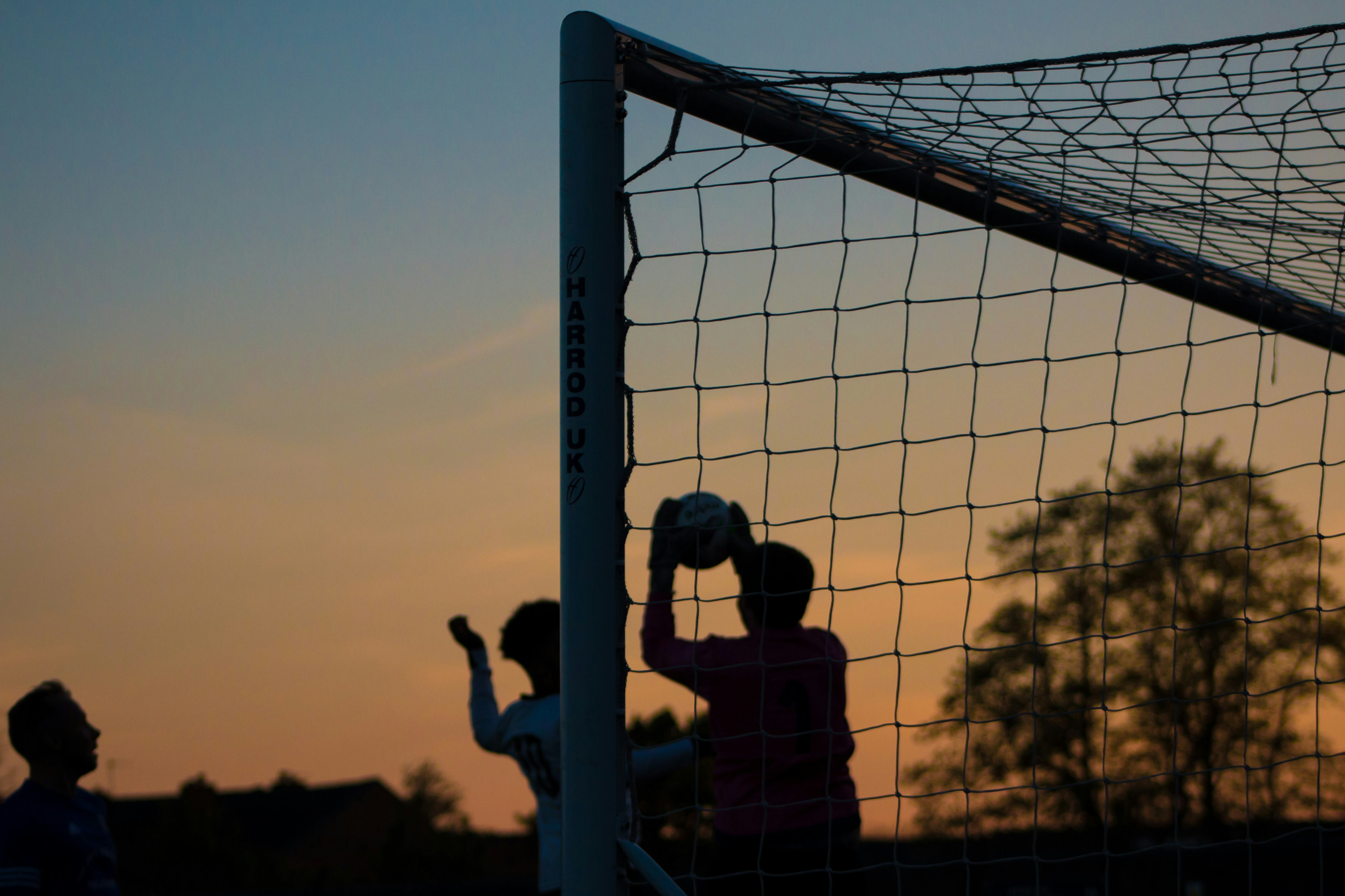 Goleiro fazendo defesa ao entardecer, silhueta contra o pôr do sol